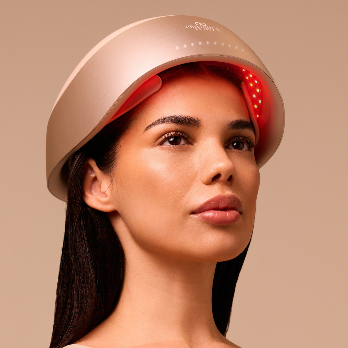 Woman wearing the LumaLase laser red light hair growth helmet, with red light glowing along her hairline